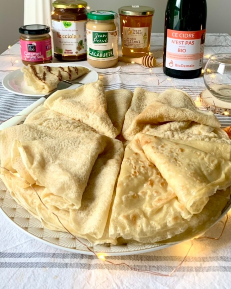 Des crêpes sont pliés en triangles sur une assiette avec des garnitures en arrière plan. 