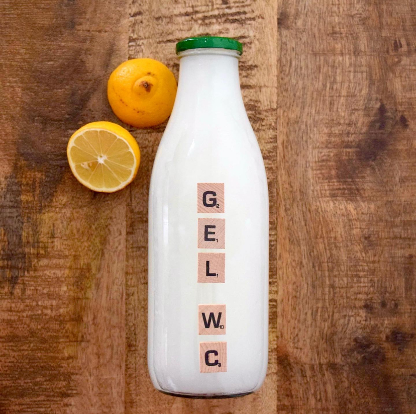 Une bouteille en verre contenant du gel WC maison est posé sur un fond en bois avec deux demi citrons posés à côté.